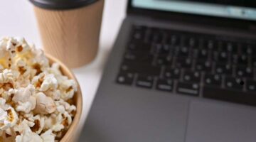 Bowl of popcorn and takeout coffee cup next to an open laptop