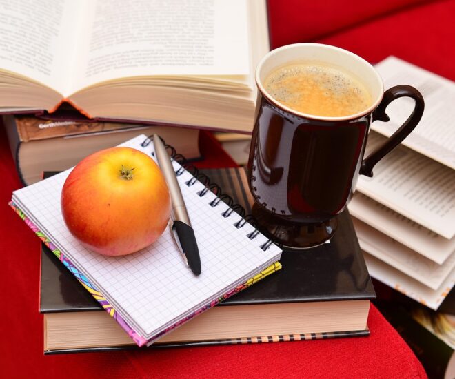 Stack of books with notebook, apple, and coffee mug on top