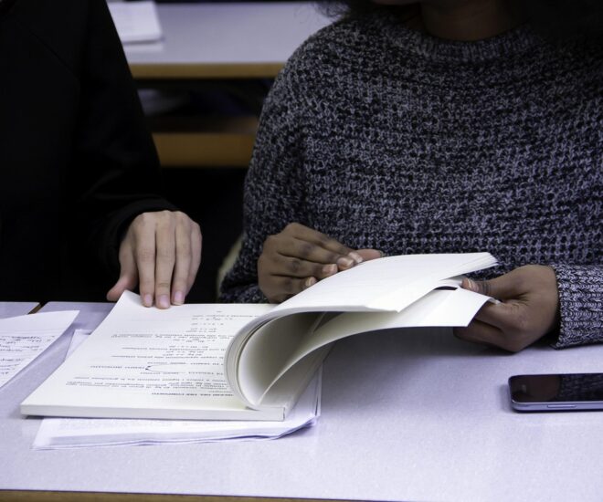 Open notebook with two female figures in front of it reviewing the content.