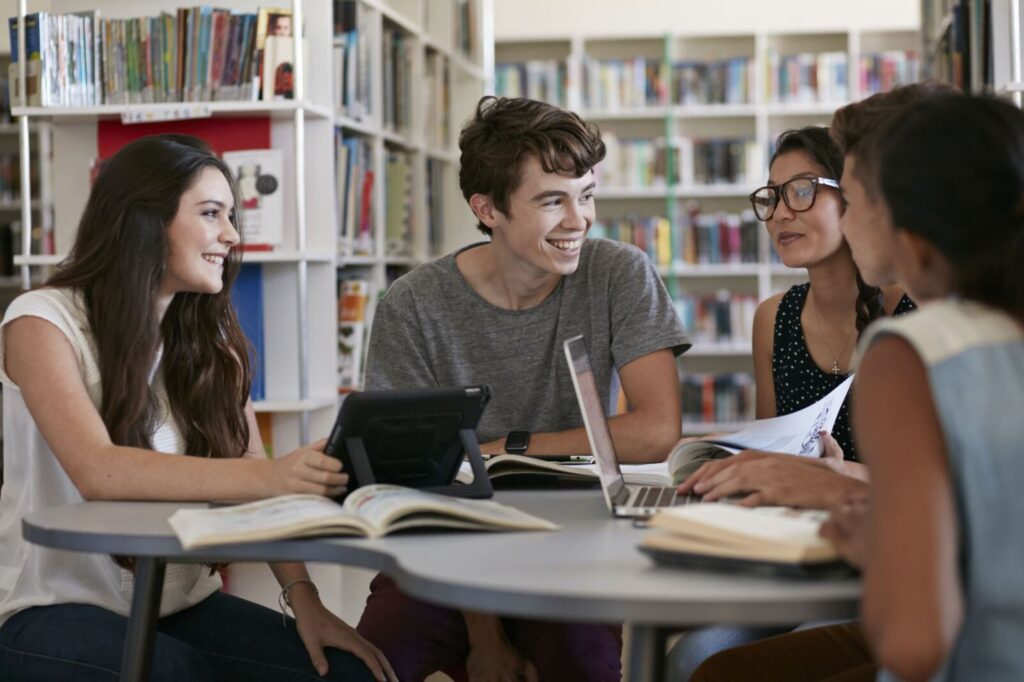 Group of students studying together with books and laptops in a library