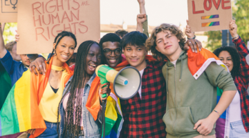 Group of people holding pride flags and signs at a rally, alongside text reading ‘Queer & Trans Resource Center, Bellevue College.’