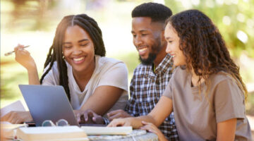 Promotional banner for the Umoja Scholars Program showing three students collaborating outdoors around a laptop