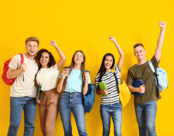 A group of five smiling young adults with backpacks standing against a yellow background.