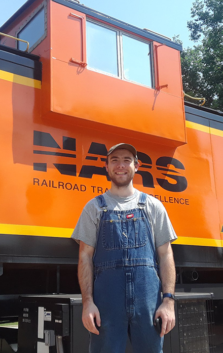An OLS alum stands in front of a train at his workplace.