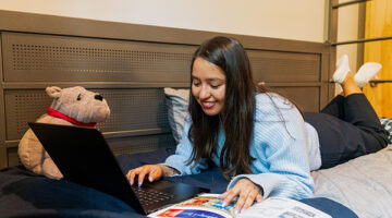 A student studies in a dorm room on campus, with a stuffed Brutus.