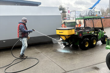 An OLS intern cleans an industrial vehicle with a hose.