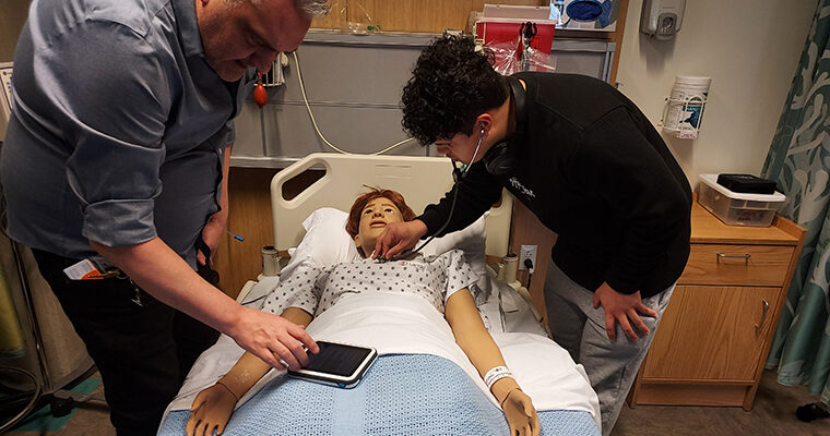An instructor teaches an OLS student how to check vital signs on a mannequin.