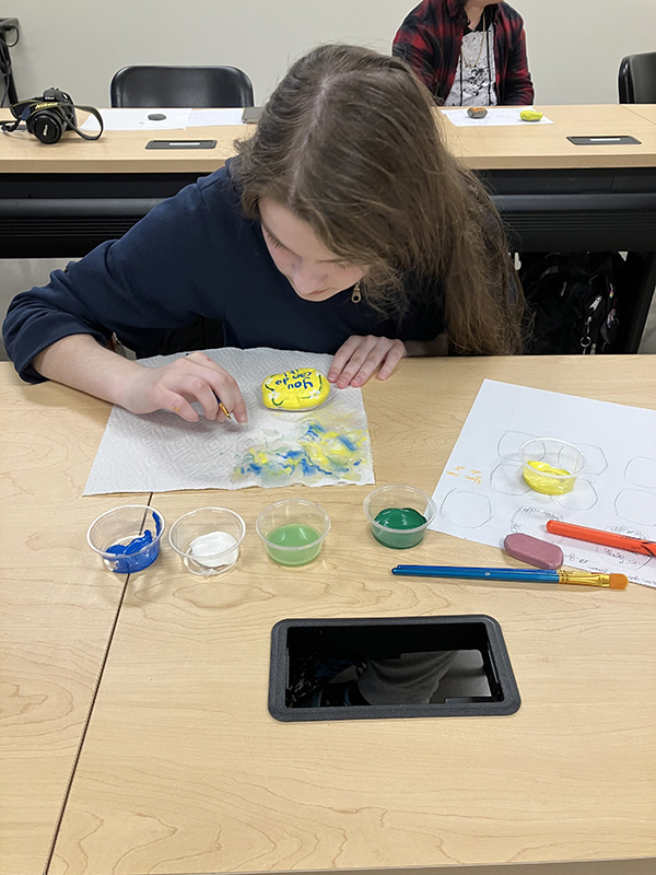An OLS student paints kindness rocks.
