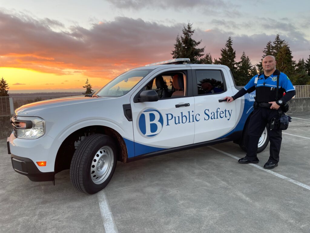 Officer in front of a white public Safety truck with sunset in the background