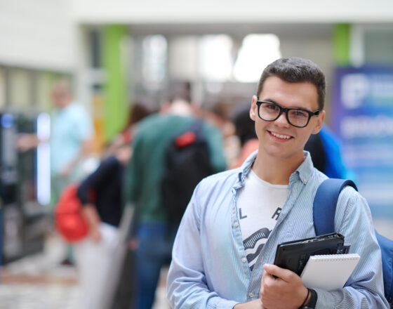 Student with backpack and laptop is smiling at the camera