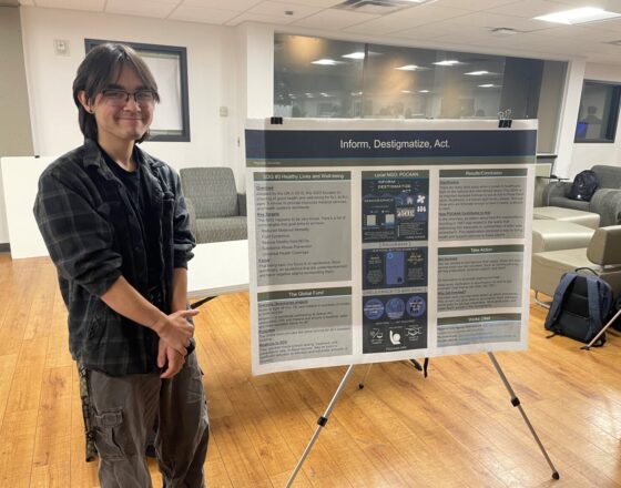 Student smiling to the camera with his showcasing project next to him