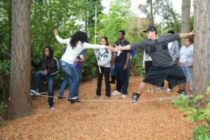 two students working together balancing on rope while other students watch