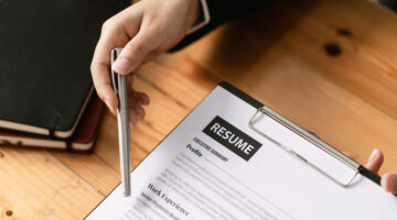 Closeup of the hand of a woman who's using a pen to point out something on a resume.