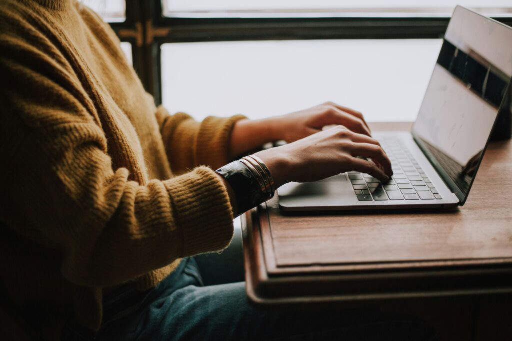 Person at a table typing on a laptop in front of windows