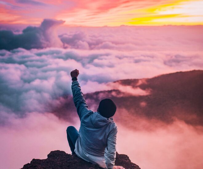 man sitting on a mountaintop above the clouds at sunset