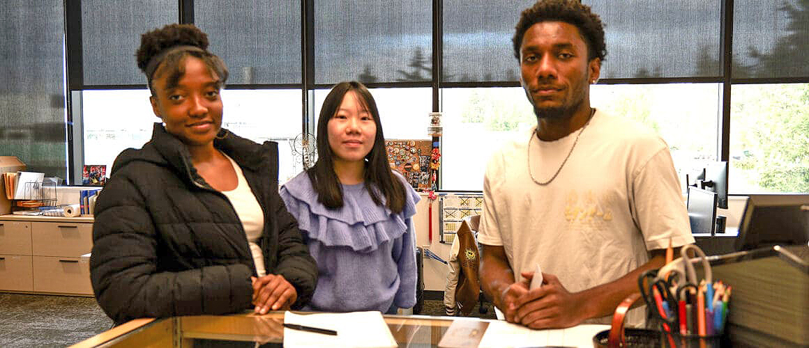 Three SBC student employees posing behind the front desk.