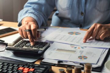 A person using a calculator while checking the numbers on a sheet
