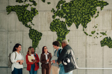 Group of diverse students smiling and discussing in front of a concrete wall with a large green moss world map