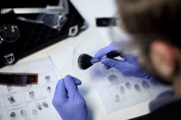 Private detective using powder and brush to take fingerprint from piece of glass
