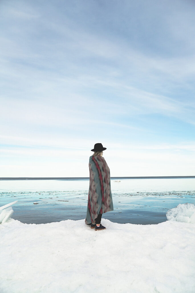 A person stands on ice while looking across the water.