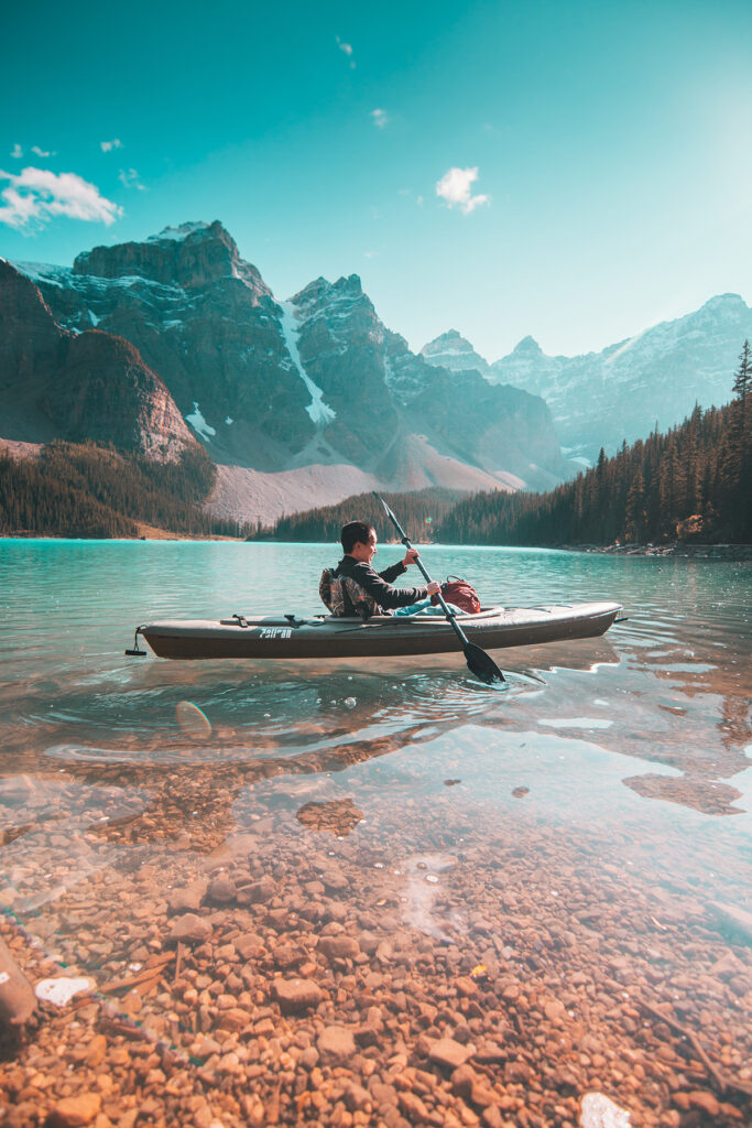 A kayaker paddles in a shallow mountain stream.