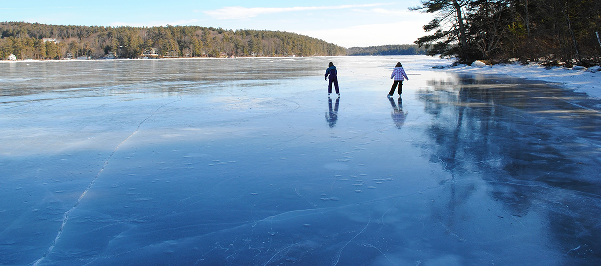 Two ice skaters skate on a glassy lake.