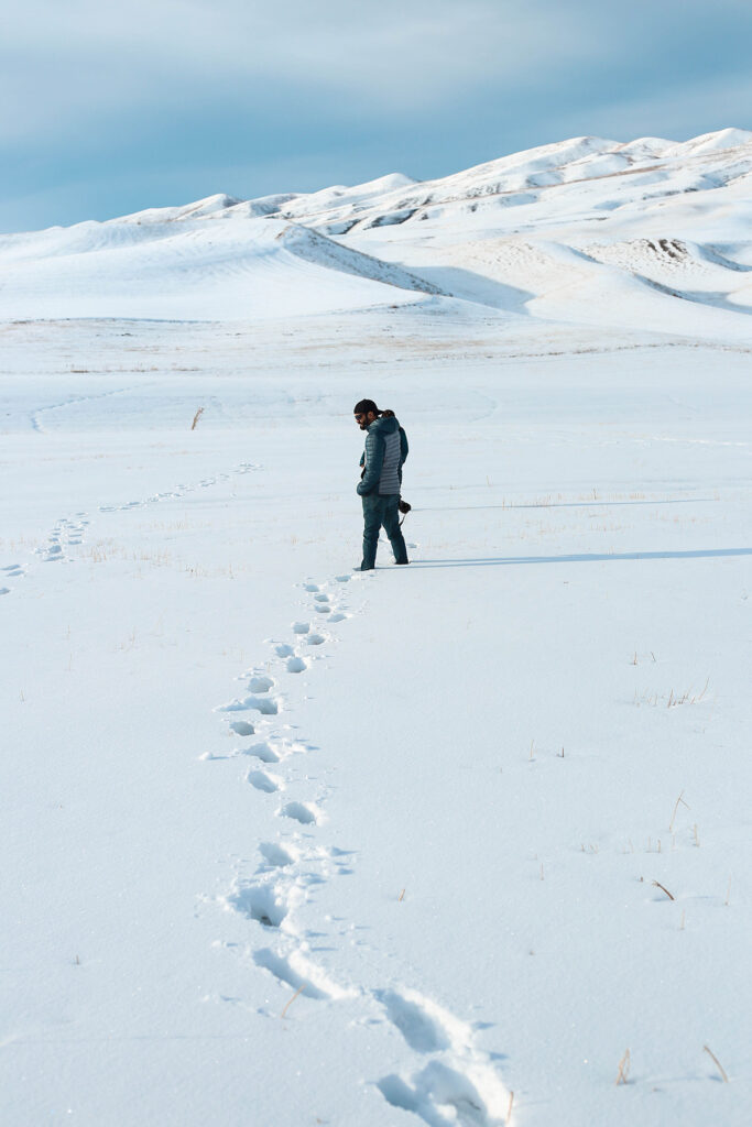 A hiker turns to look at footprints in the snow.