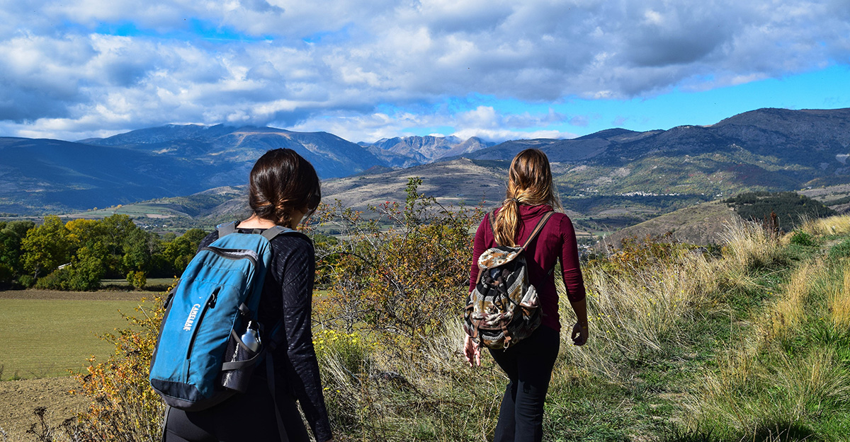 Two hikers follow a trail through a meadow, heading toward the foothills.