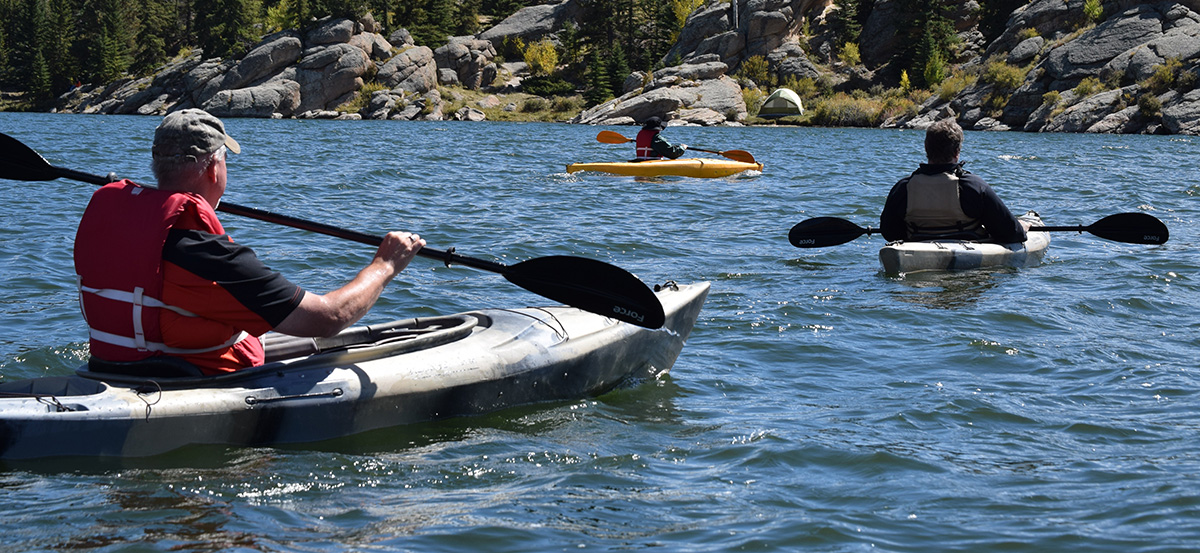 Kayakers paddle along a rocky coast.