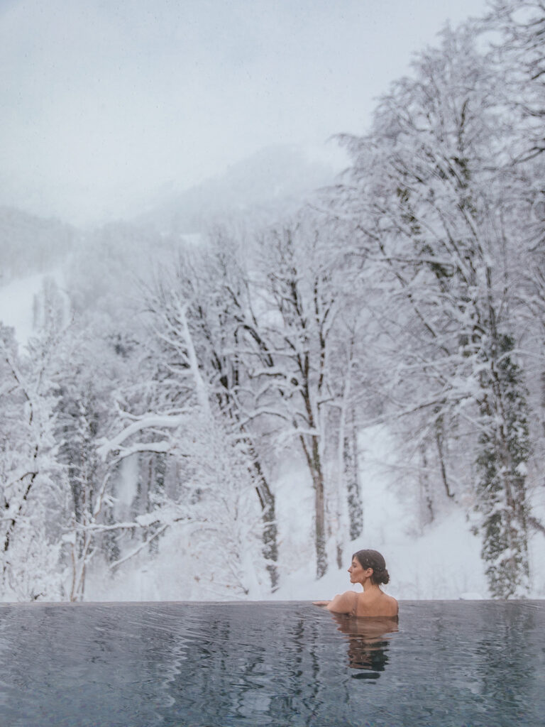 A winter swimmer enjoys the icy water, surrounded by snowy trees.