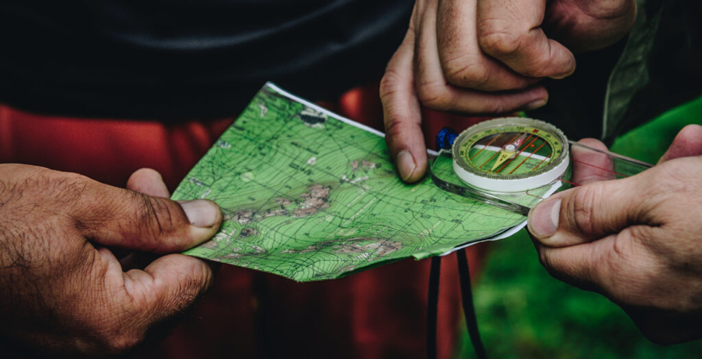 Hands using a compass and a map with forest in the background.