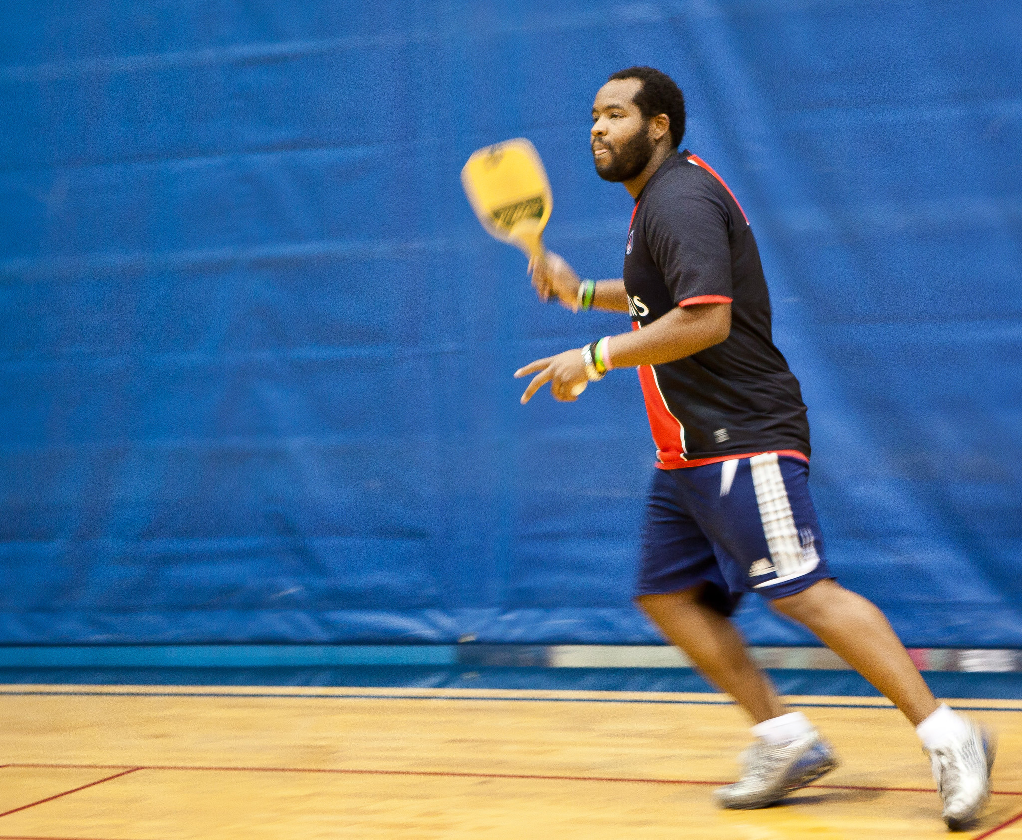 Male student playing pickleball and leaning towards the ball.
