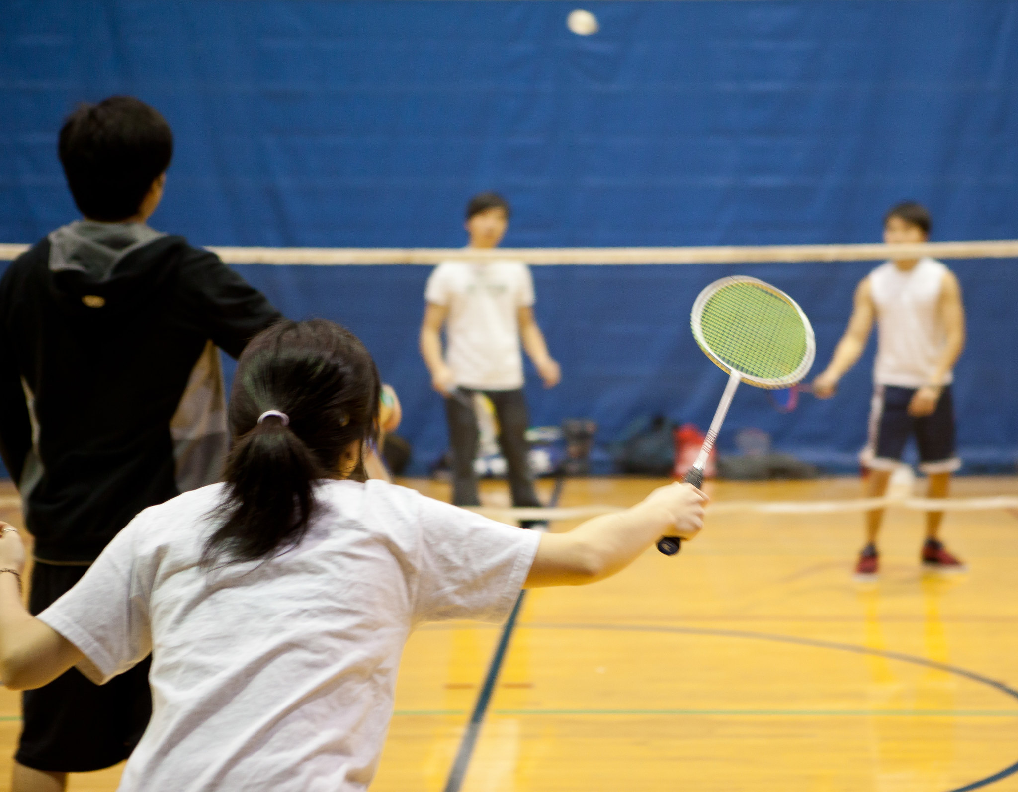 Female student serving over the net in doubles badminton game