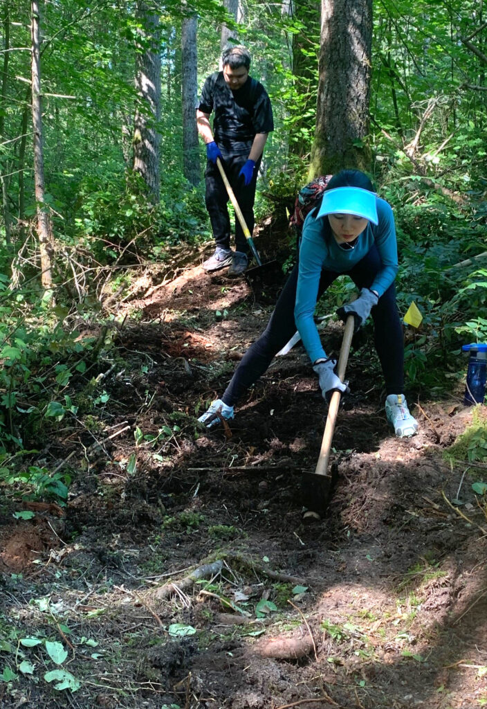 Two young trail workers using manual tools to improve the trail.