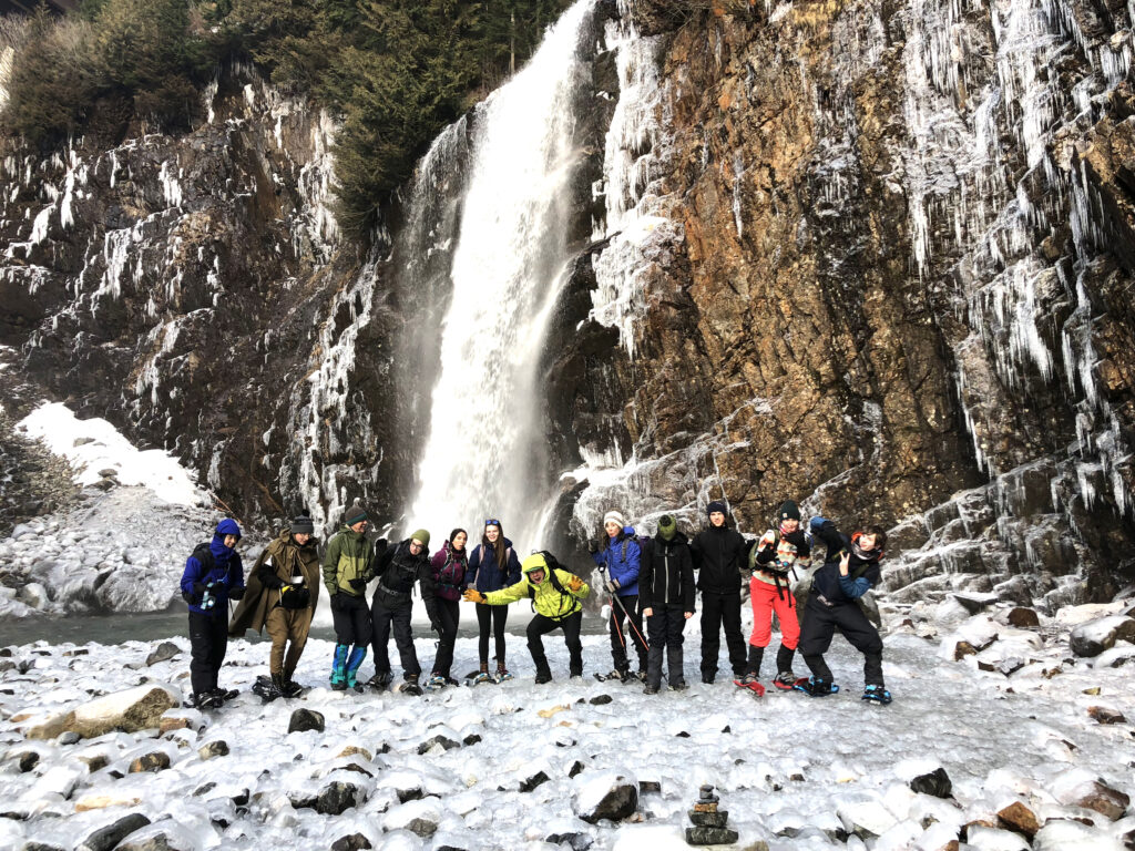 A team of about a dozen students kitted out in snow gear standing in front of Franklin Falls in the snow.