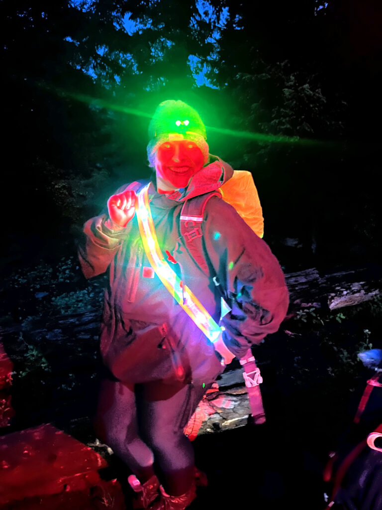 Student modeling their headlamp and reflective runner's straps as the sun goes down on an overnight backpack.