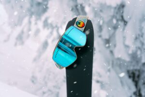 Ski goggles hanging on the tip of a ski with snowy background