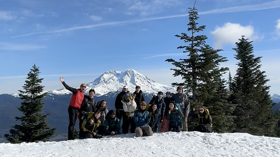 Group photo, snowshoeing under blue skies and Mt Rainier in the distance.