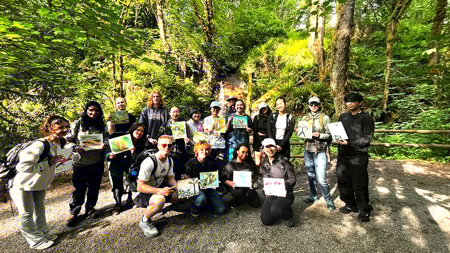 Students on an Art Hike, posing next to a lush forest ravine with their paintings of the forest.