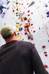 Climber on the rock wall, harnessed and roped up with instructor holding the rope.