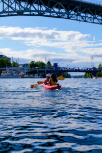 Kayaking on Lake Union under the ship canal bridge with blue water, blue skies and white fluffy clouds.