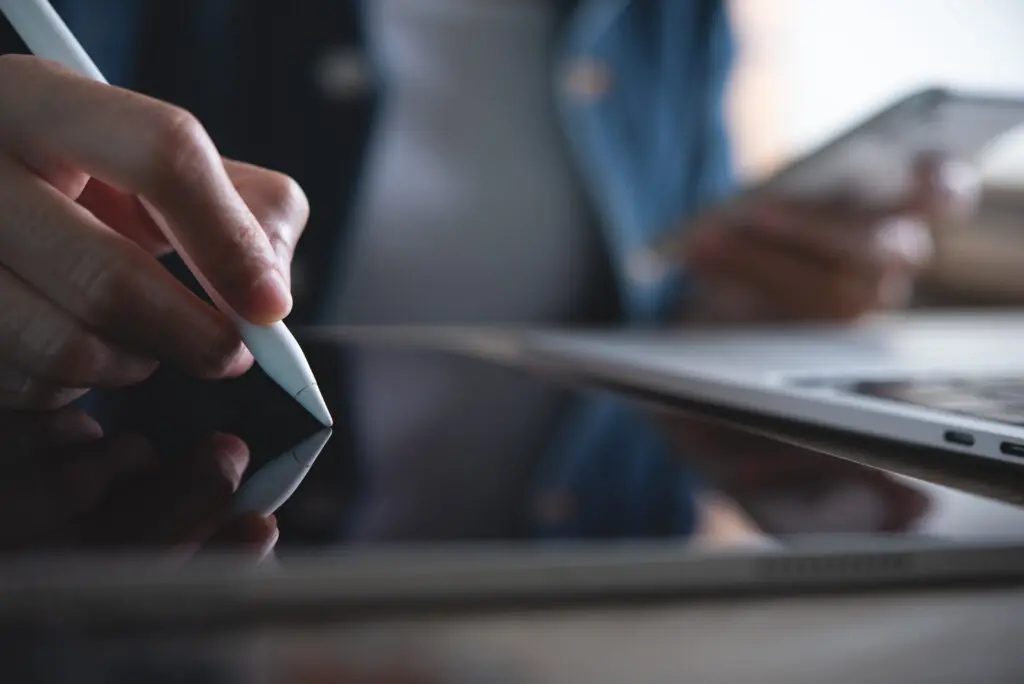 This image has an empty alt attribute; its file name is AdobeStock_483544765-1024x684.jpegClose up of business woman hand with stylus pen working on digital tablet pc and laptop computer on office table, using mobile phone at home, Student studying online class. E-learning, telecommuting concept