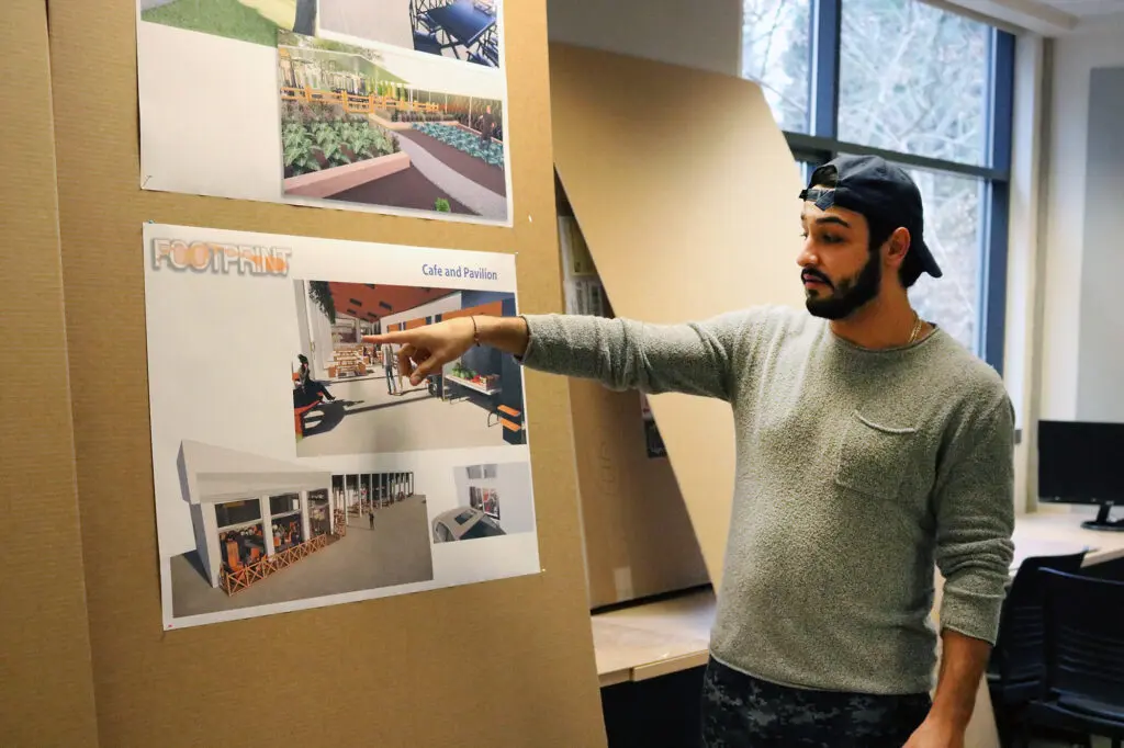 A student gestures to a poster with interior designs.