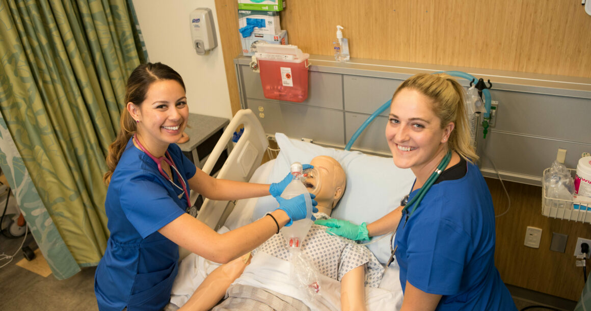 Two nursing students working with a dummy in the T Building lab