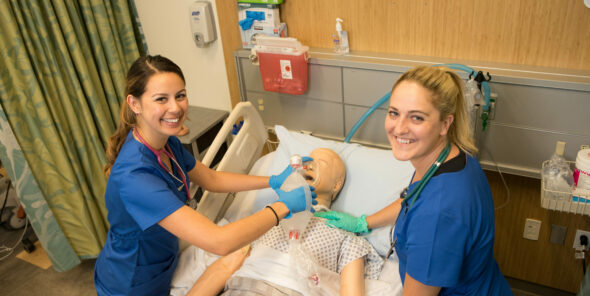 Two nursing students working with a dummy in the T Building lab