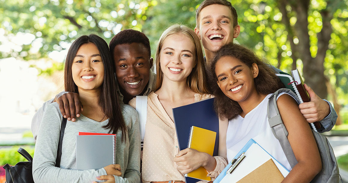 Group of international happy students with books and notebooks having fun in park after studying, smiling at camera