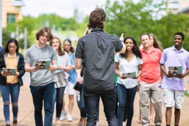 I group of students and parents outside walking together and a tour guide leading them.