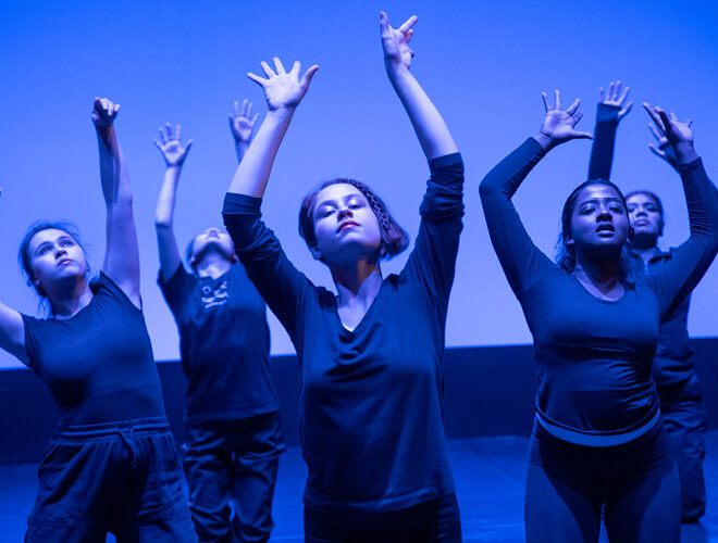 Dancers stretch and reach together on-stage.