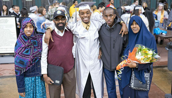 A BC grad in a white gown poses with family or friends before the ceremony