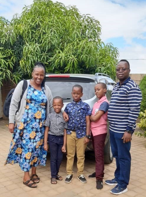 Dr. Moshi smiling with her husband and three children standing in front of a big tree and a vehicle.